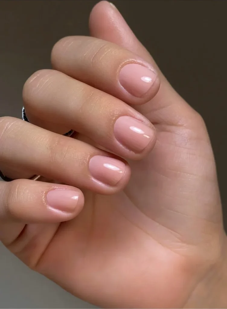 Main aux ongles courts portant un vernis rose nude, finition naturelle
