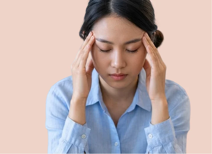 Femme en chemise bleue, les yeux fermés, les doigts posés sur les tempes