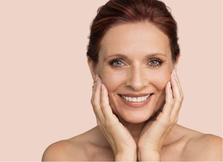 Femme souriante d'une cinquantaine d'années, le visage entre les mains