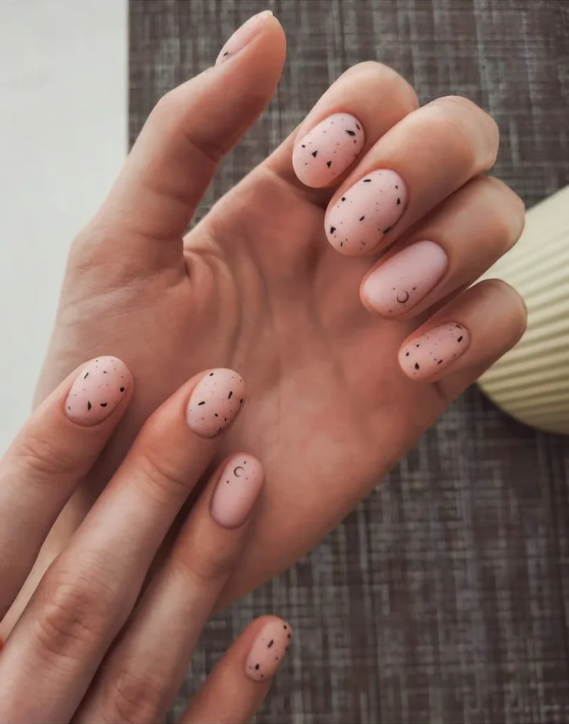 Mains aux ongles courts décorés de petits motifs discrets, vernis nude