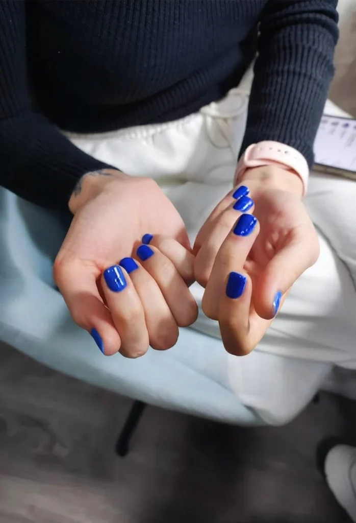 Mains aux ongles vernis bleu vif, posées sur les genoux